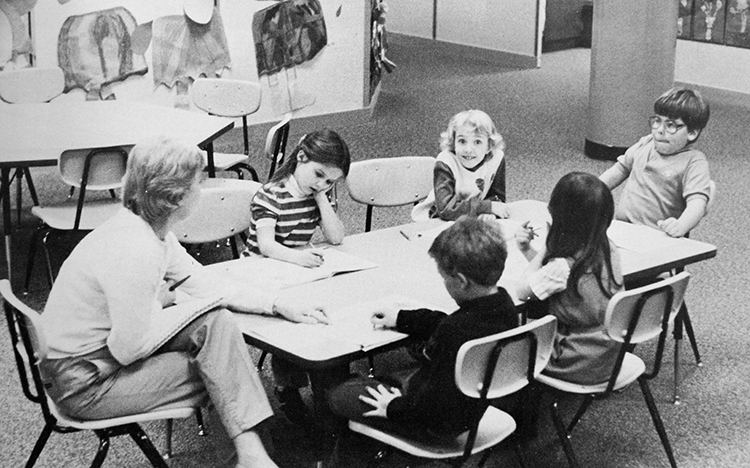 Black and white yearbook photograph of a small group of students working around a table with a teacher.