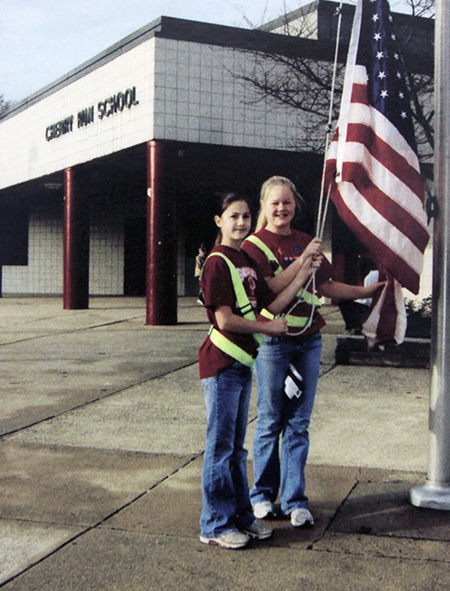 Yearbook photograph of two safety patrol officers raising the American flag in front of Cherry Run Elementary School.